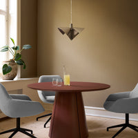 Gray upholstered chairs around a round, rust-colored table with a modern pendant light in a warm-toned room.