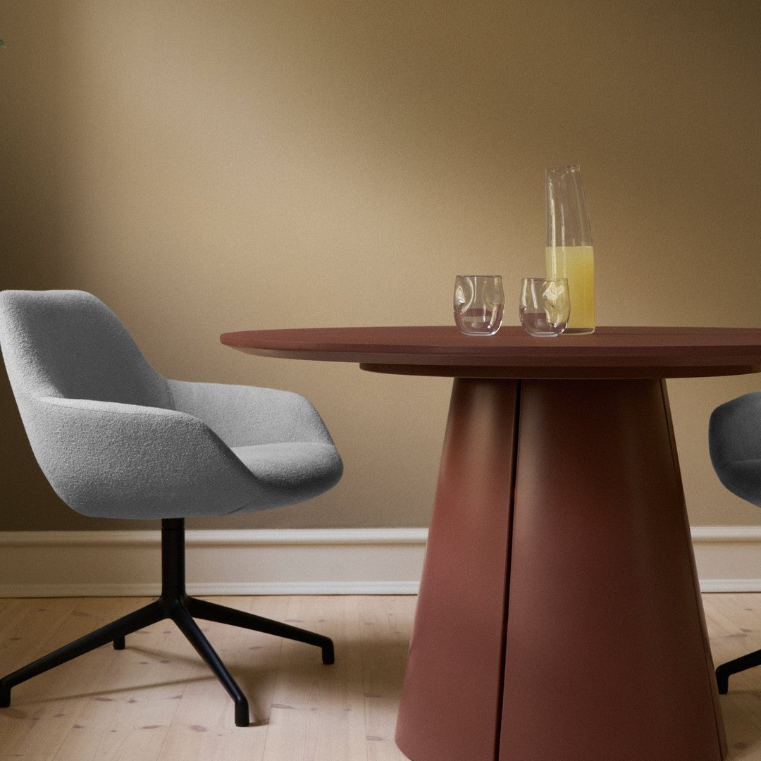 Grey upholstered chairs and a brown circular table against a warm beige wall, featuring minimalistic design.