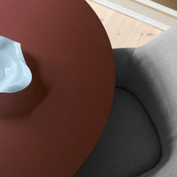 Round rust-colored table with a soft gray chair, featuring a glossy blue vase on top. Modern minimalist design.