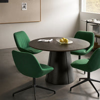 Round black tabletop with sleek base, surrounded by four vibrant green upholstered chairs. Clean, modern aesthetic.