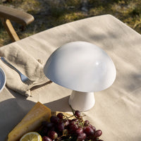 White glossy mushroom-shaped lamp on a sandy table setting, surrounded by grapes and cheese. Soft and modern design.