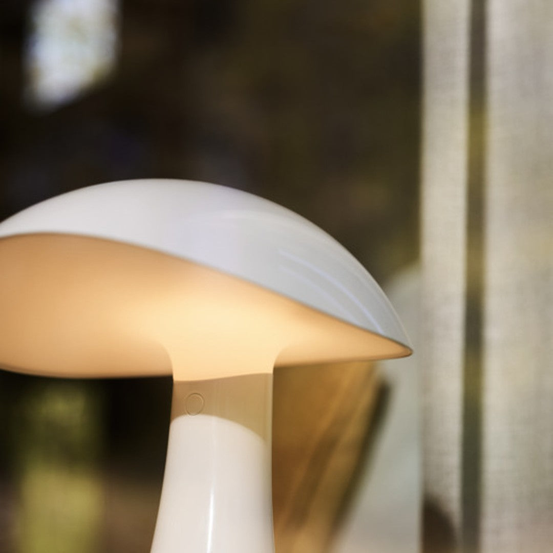 White and soft beige lamp with a smooth, rounded shade and minimalist design against a blurred background.