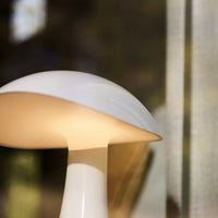 White and soft beige lamp with a smooth, rounded shade and minimalist design against a blurred background.