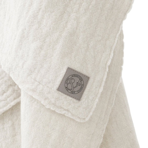 Cream textured fabric with subtle pattern and a gray logo patch detailing, perfect for cozy indoor styling.