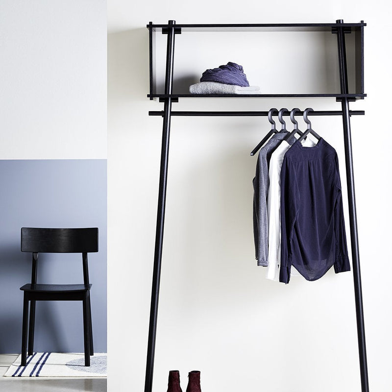 Minimalist black clothing rack with navy and white garments against a light gray wall, complemented by a black chair.