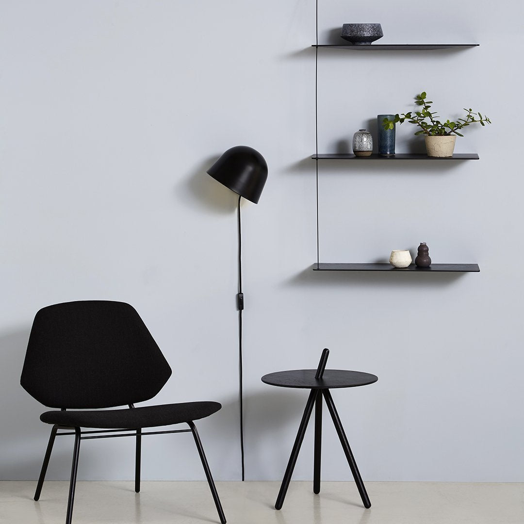 Black chair and lamp against a pale blue wall, featuring sleek black shelves and minimalistic decor.