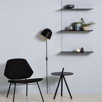 Black chair and lamp against a pale blue wall, featuring sleek black shelves and minimalistic decor.