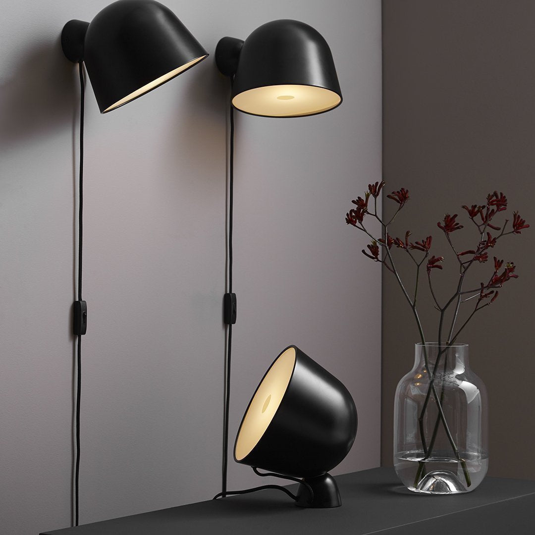 Black matte lamps with soft golden interiors, minimalist design against a neutral wall, featuring sleek lines and modern elegance.