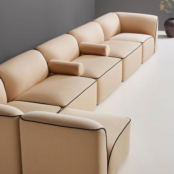 Beige sectional sofa with smooth fabric and contrasting black piping, featuring a modern and minimalist design.