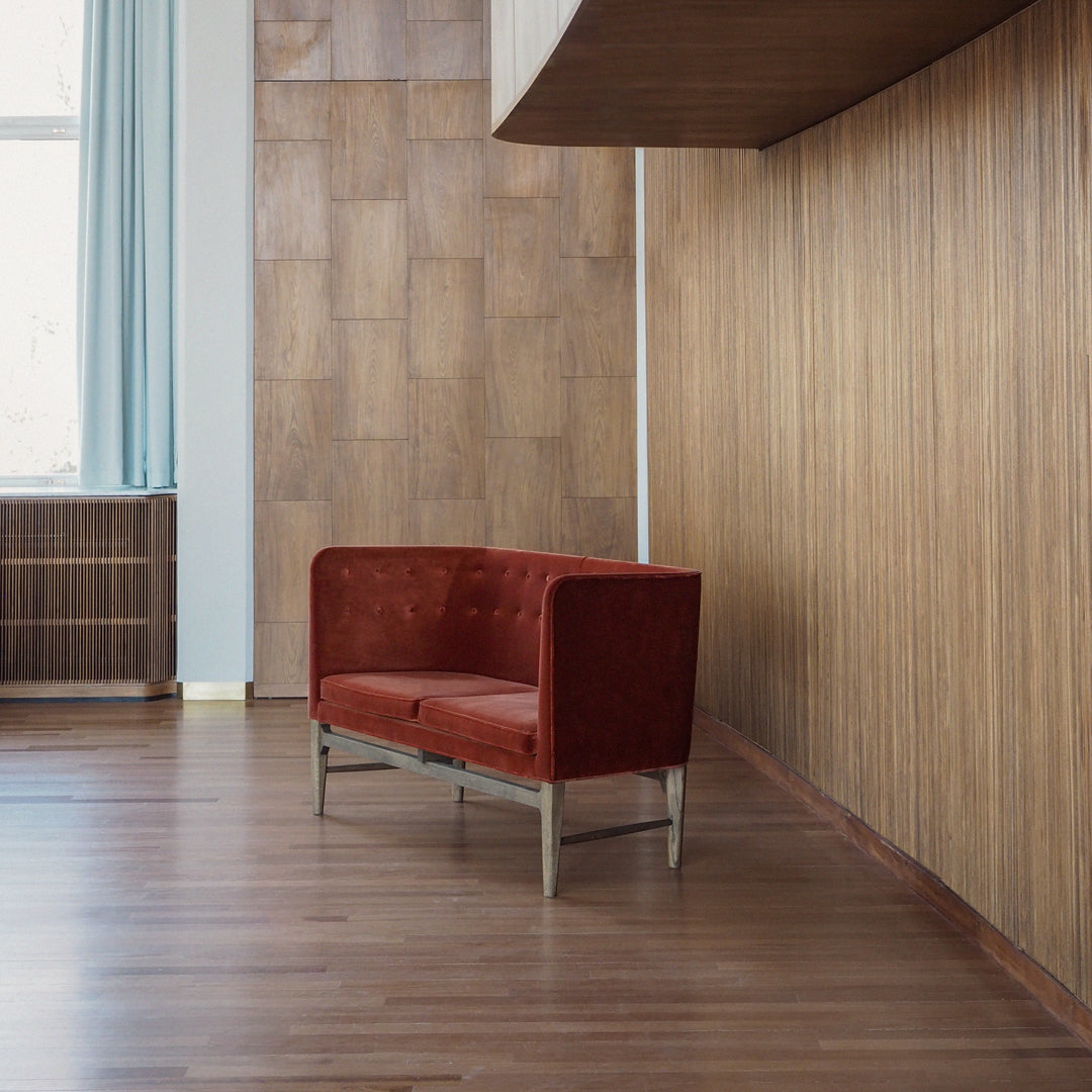 Red velvet sofa against a wooden wall, featuring a sleek modern design and stylish metal legs.