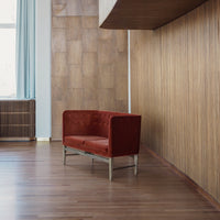 Red velvet sofa against a wooden wall, featuring a sleek modern design and stylish metal legs.