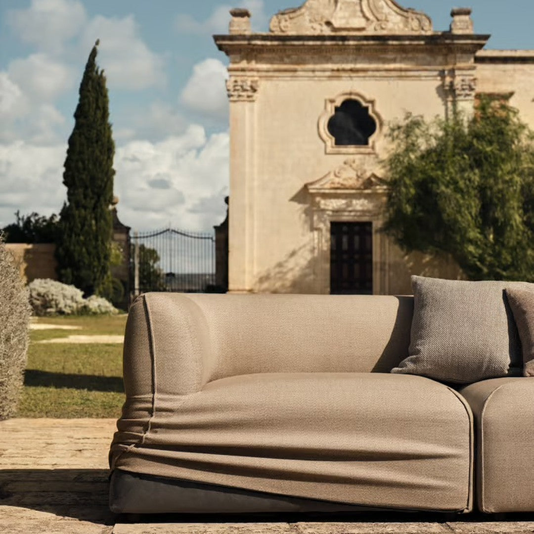 Beige textured sofa with smooth fabric and casual draping, set against a stylish outdoor backdrop.