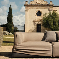 Beige textured sofa with smooth fabric and casual draping, set against a stylish outdoor backdrop.