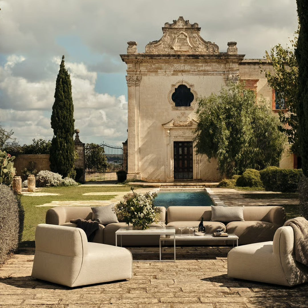 Elegant outdoor sofa set in neutral tones, featuring soft beige upholstery and minimalist design against a rustic backdrop.