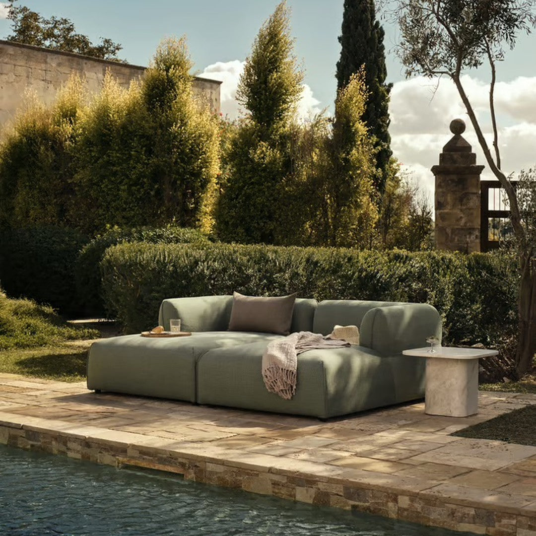 Modern outdoor sofa in soft sage green, featuring a smooth, minimalist design against a lush garden backdrop.