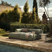 Modern outdoor sofa in soft sage green, featuring a smooth, minimalist design against a lush garden backdrop.