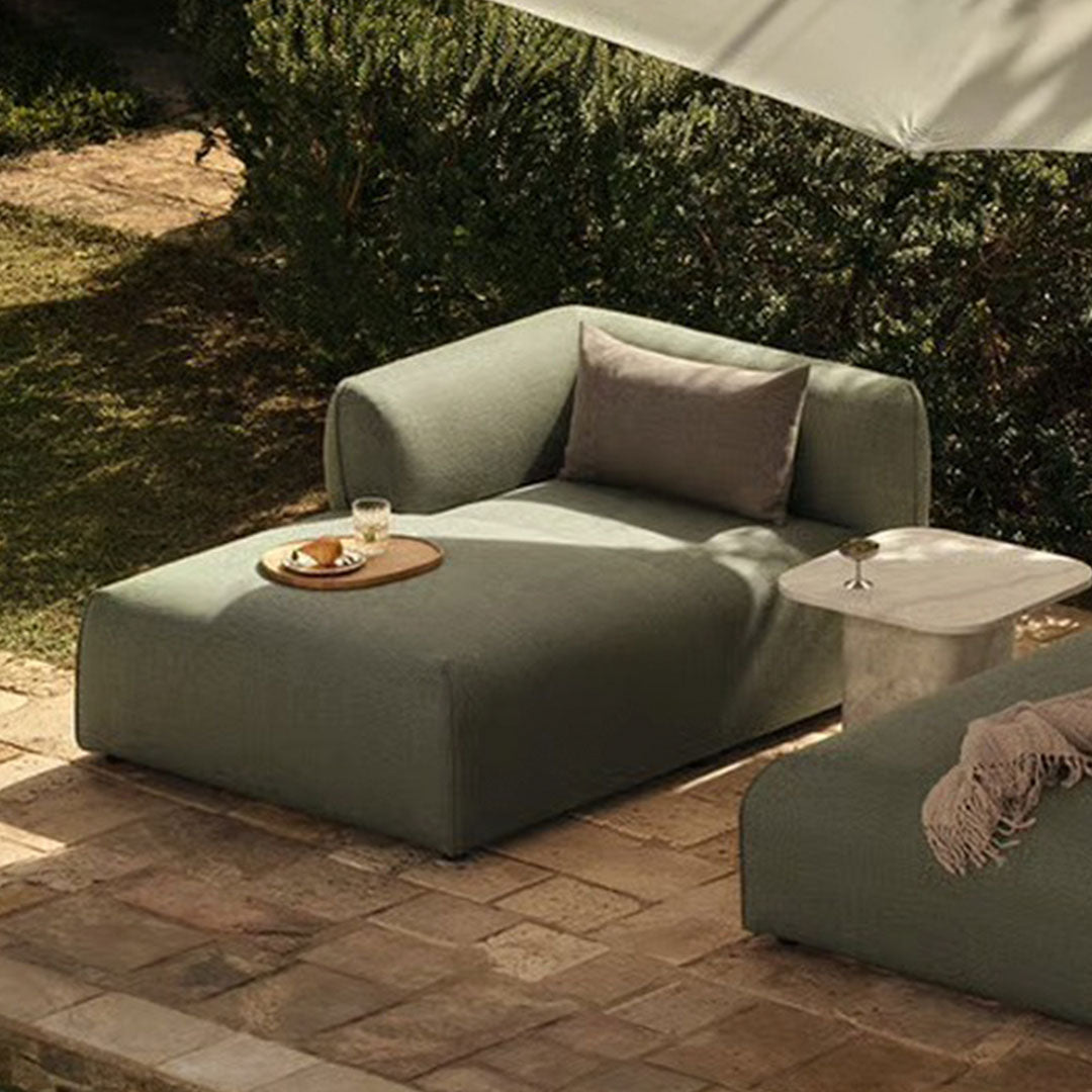 "Light green chaise lounge with clean lines and soft, minimalist design on a stone patio."
