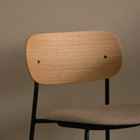 Natural wood finish backrest with black metal frame and textured beige upholstery seat. Simple, modern design.