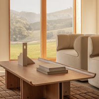 Light wood coffee table with smooth edges, set against a neutral-toned sofa and a textured brown rug. Natural light ambiance.