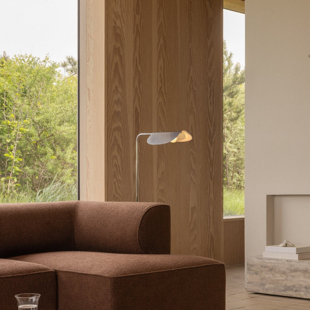 Brown fabric sofa with a sleek metal lamp, complemented by a natural wood backdrop and greenery outside.