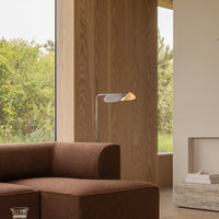 Brown fabric sofa with a sleek metal lamp, complemented by a natural wood backdrop and greenery outside.