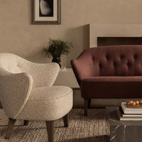 Cream textured armchair and deep burgundy tufted loveseat against a neutral-toned wall, accented by natural elements.