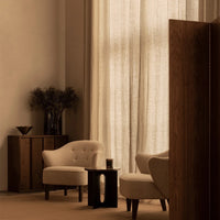 Cozy beige armchairs and a dark wood table against soft, warm neutral tones and textured curtains.