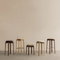 Collection of five stylish bar stools in muted colors: dark brown, light beige, olive green, and creamy white.