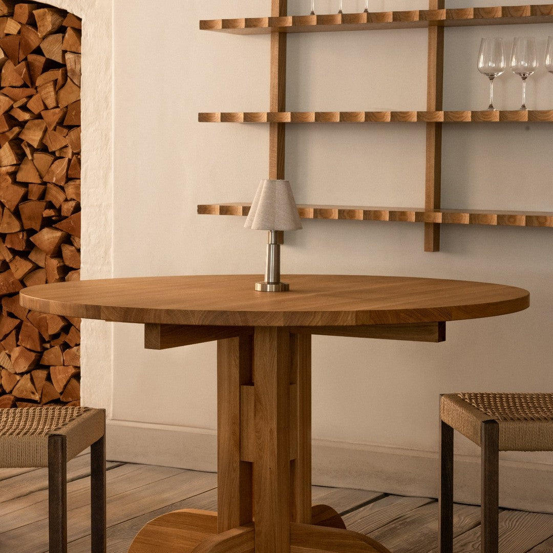 Wooden round table with a natural oak finish, paired with woven chairs against a simple, light backdrop.