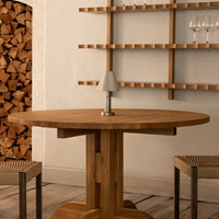 Wooden round table with a natural oak finish, paired with woven chairs against a simple, light backdrop.