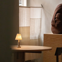 Neutral-toned, textured fabric screen with warm beige and soft cream colors, paired with a wooden table and lamp.