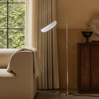 Sleek, modern floor lamp with a white shade and silver base, set against warm beige decor and natural light.