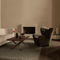Elegant beige sofa and gray armchair on a soft green rug, complemented by a wooden table and neutral wall tones.