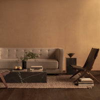 Beige upholstered sofa, dark marble coffee table, brown wooden chairs, and neutral rug against warm-toned walls.
