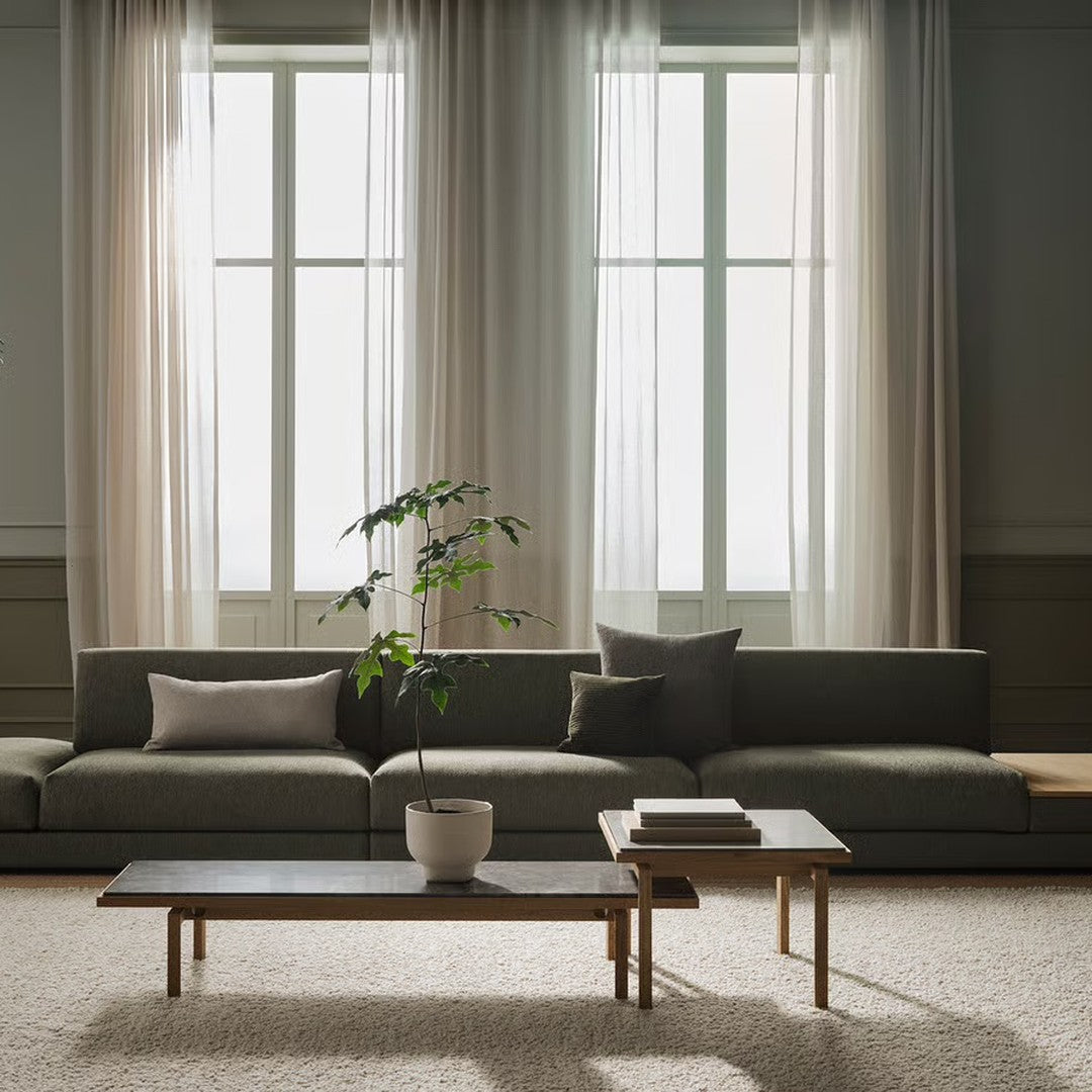Modern grey sectional sofa with light beige cushions and a wooden coffee table in a bright, airy room with sheer curtains.