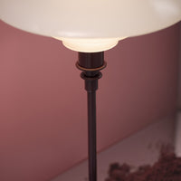 Elegant white lamp shade with a sleek dark metal base, set against a soft pink background. Modern design aesthetics.