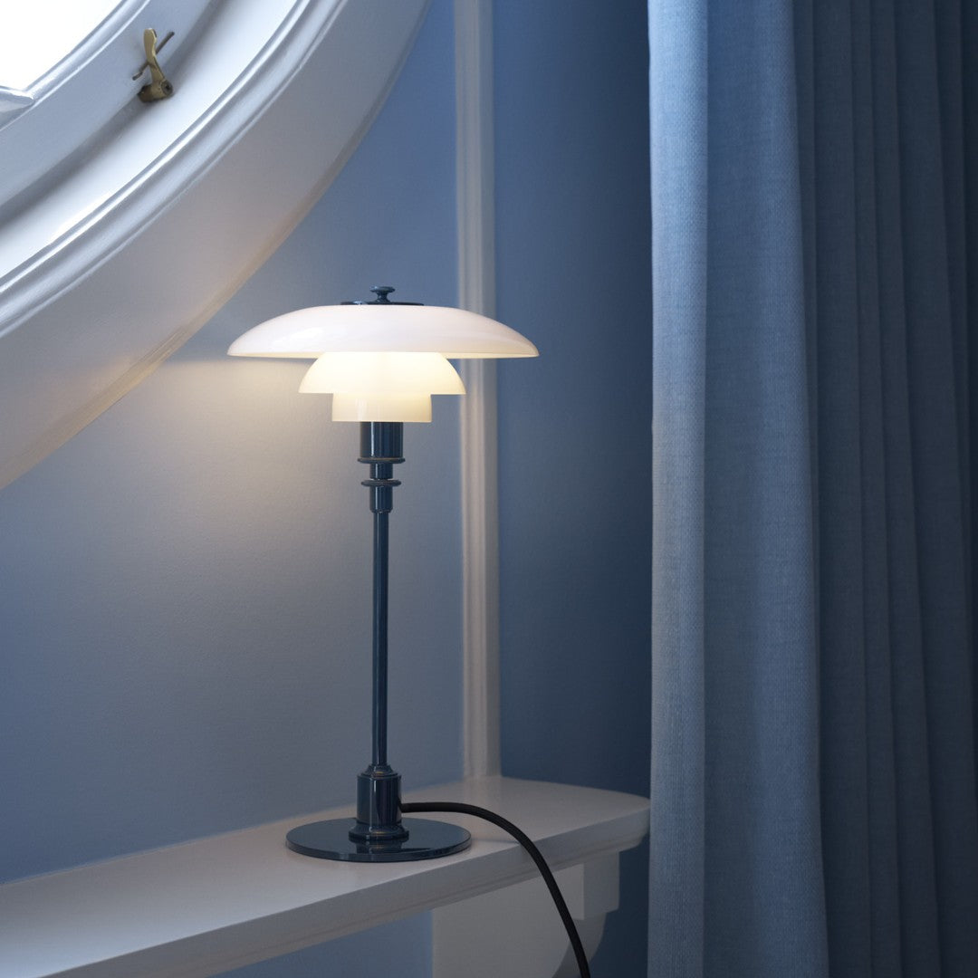 Modern table lamp with a sleek blue base, white glass shade, and soft blue curtains in a light blue room.
