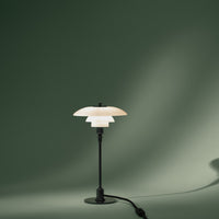 Elegant black metal lamp with a layered white shade, set against a soft green backdrop. Modern design with minimalist appeal.
