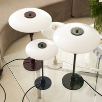 "Set of four modern table lamps featuring white glass shades, green, burgundy, and black bases on a glass table."