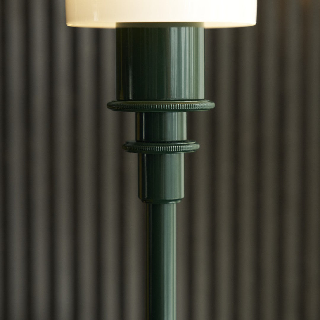 Green ribbed lamp base with a glossy finish, topped by a soft white lampshade, set against textured striped background.