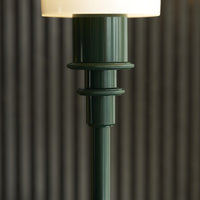 Green ribbed lamp base with a glossy finish, topped by a soft white lampshade, set against textured striped background.