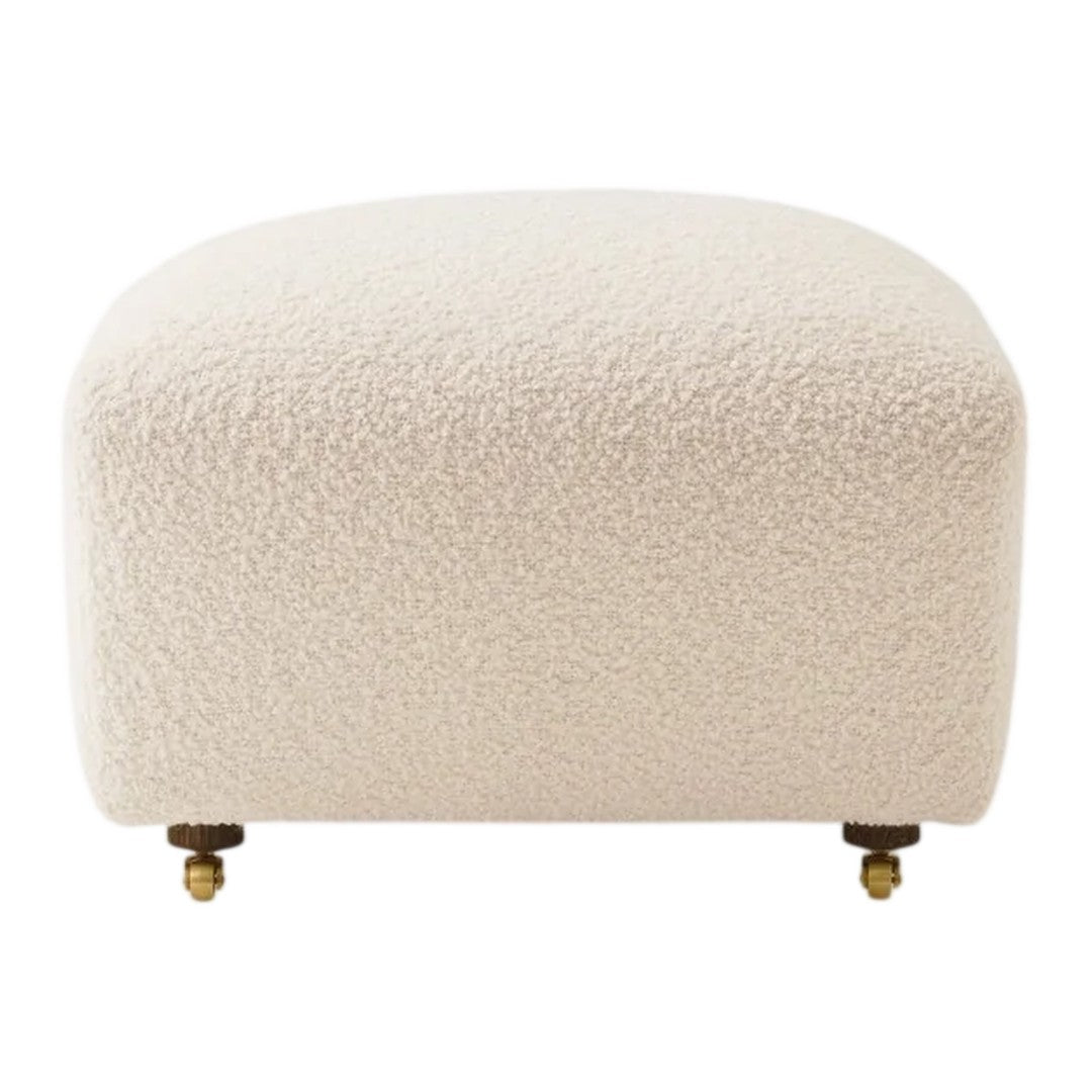 Cream-colored ottoman with a textured, boucle fabric and brass accents on short legs.