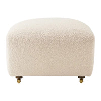 Cream-colored ottoman with a textured, boucle fabric and brass accents on short legs.