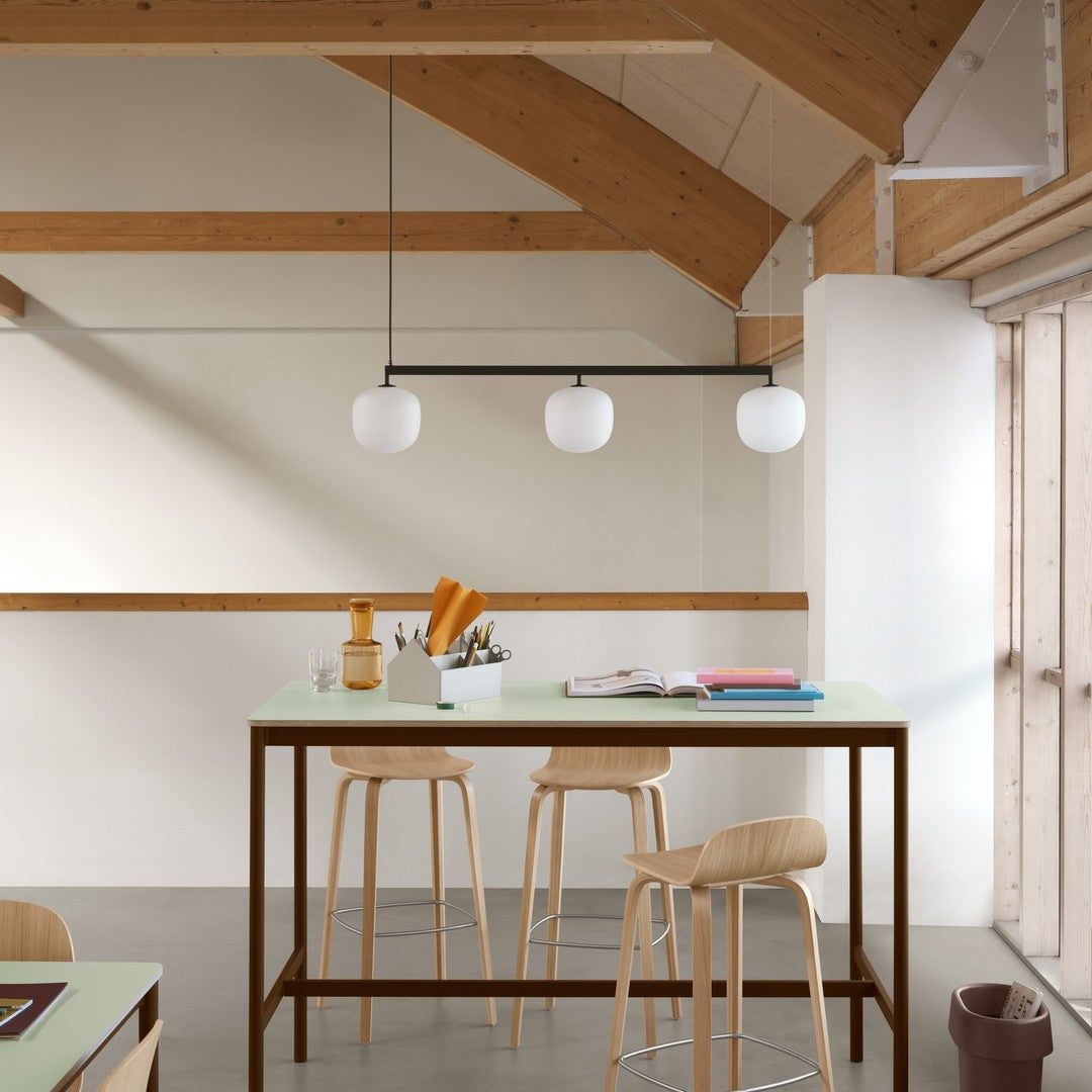 Modern kitchen with natural wood accents, white pendant lights, and a mint green table, featuring sleek, minimalist design.