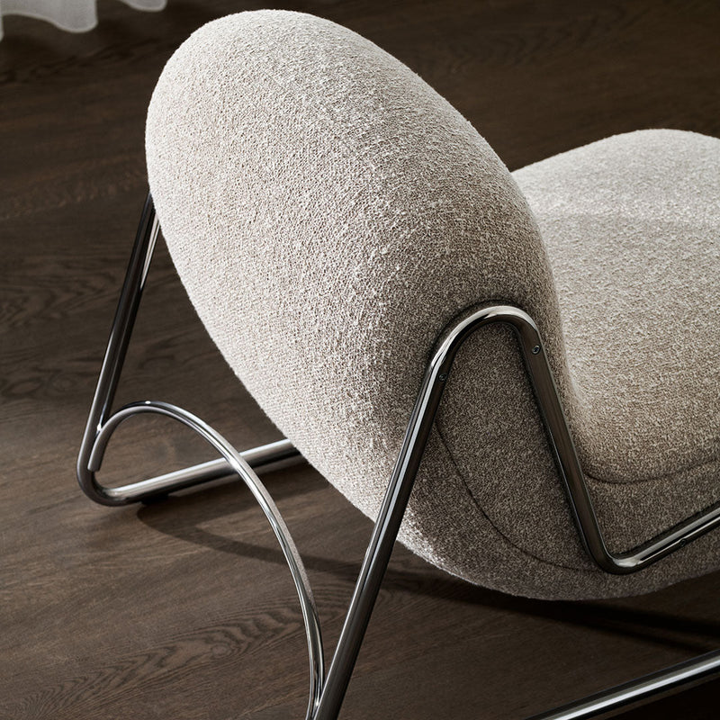 Beige textured chair with rounded shape and sleek chrome legs on a dark wood floor. Modern and minimalist design.