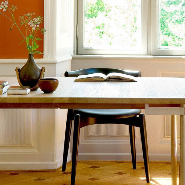 Elegant black chair and wooden table set against warm orange walls and natural light, featuring minimalist decor.