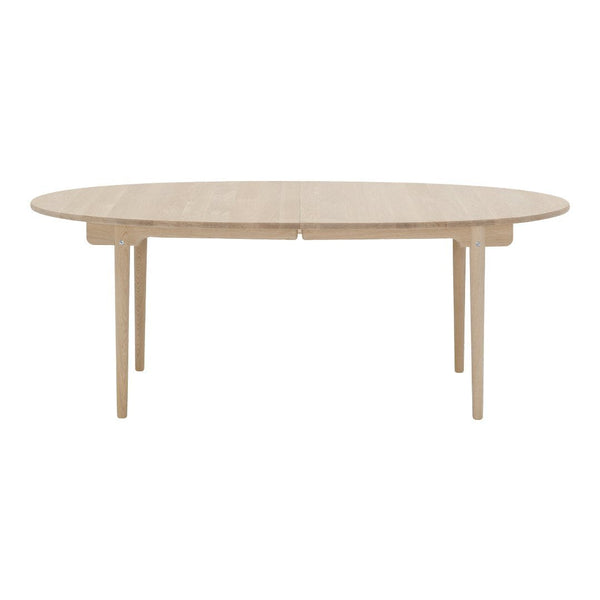 Light beige oval dining table with a smooth, minimalist surface and natural wood grain, supported by sleek legs.