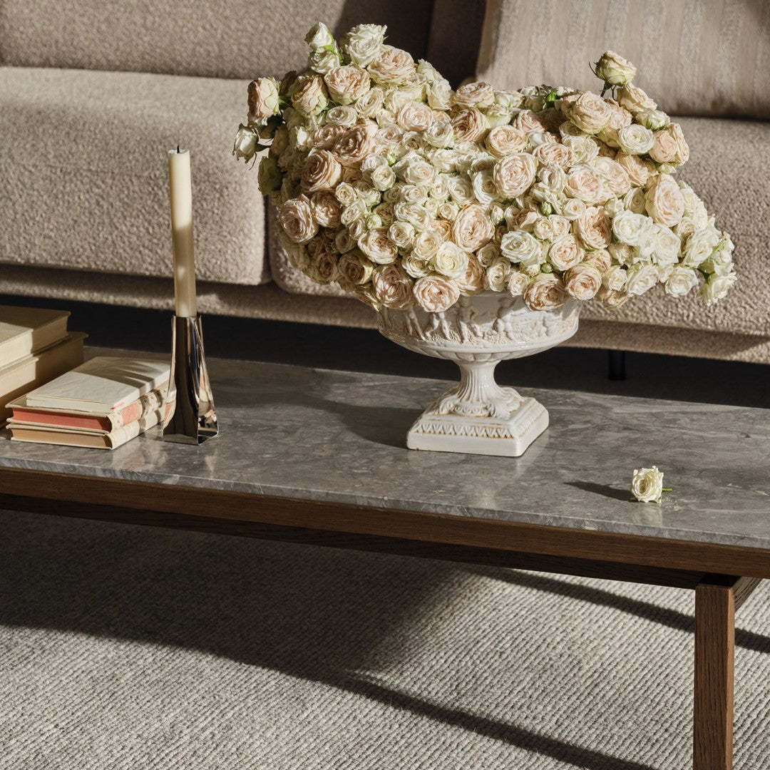 "Elegant floral arrangement in soft beige and cream hues on a textured gray tabletop, complemented by a sleek candle holder."