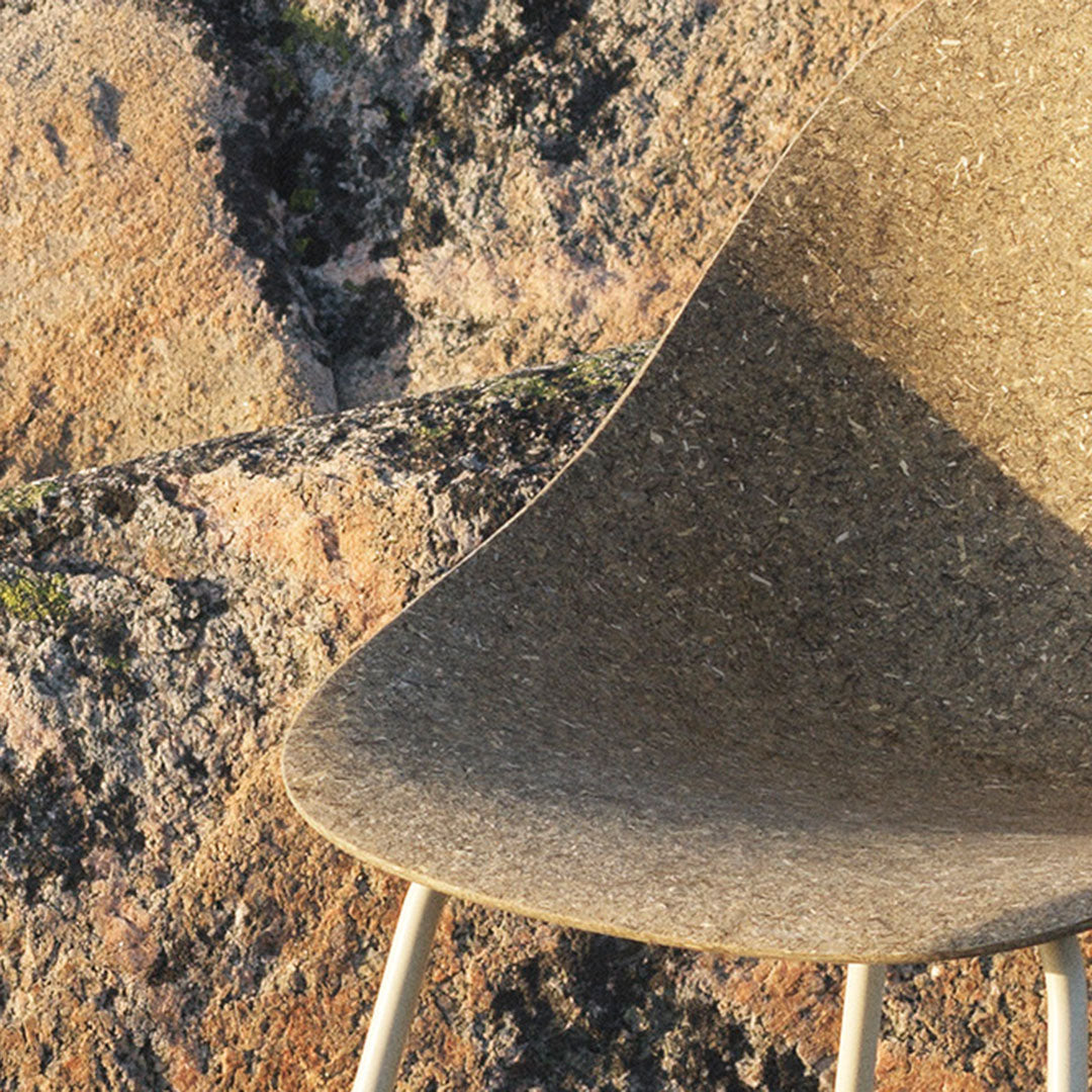 Smooth, earthy brown chair against a textured stone background; minimalist design with natural hues.