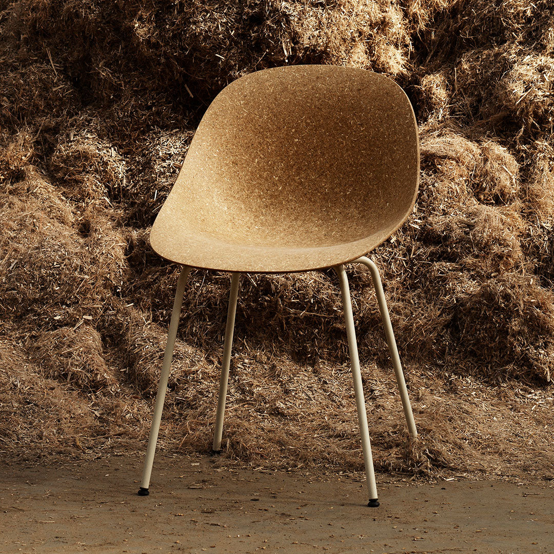 Cork-colored chair with a smooth, organic shape and metallic legs, set against a textured brown backdrop.